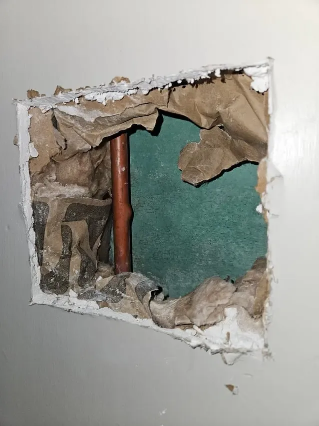 Copper pipe visible through a controlled opening in a wall