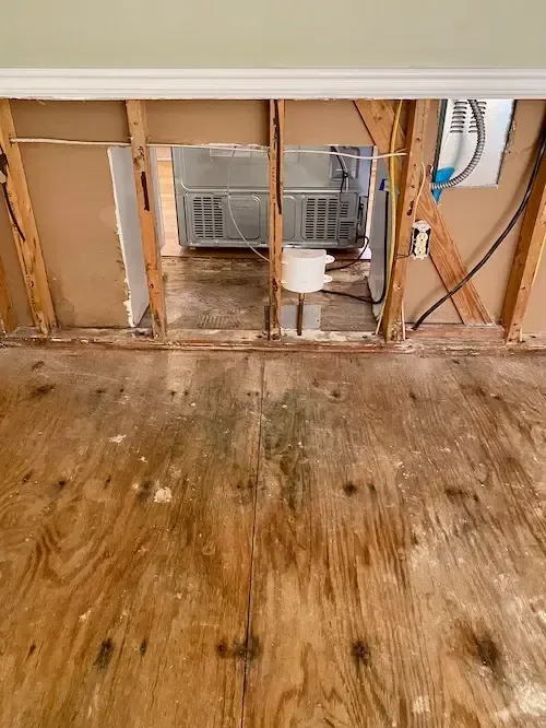 Wood subfloor exposed beneath an opened wall cavity