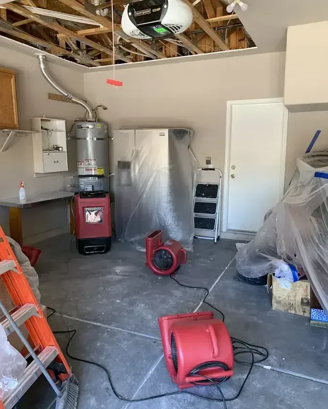 Red air movers beside a water heater beneath an opened ceiling