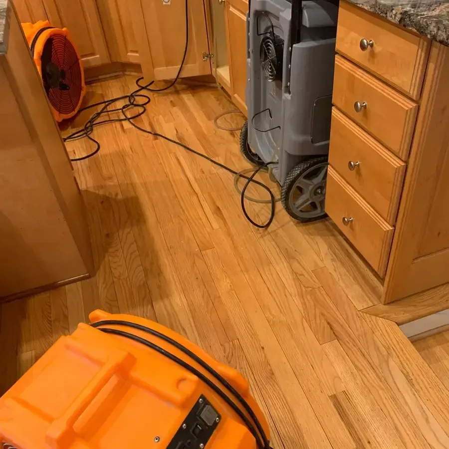 Air mover and dehumidifier drying a kitchen with hardwood flooring