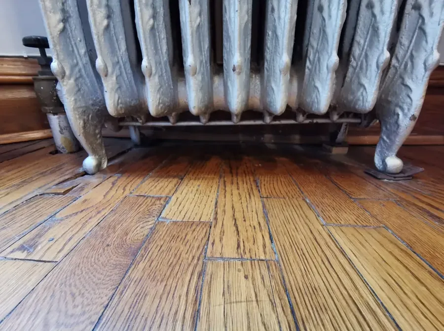 Darkened oak floorboards beneath a cast iron radiator